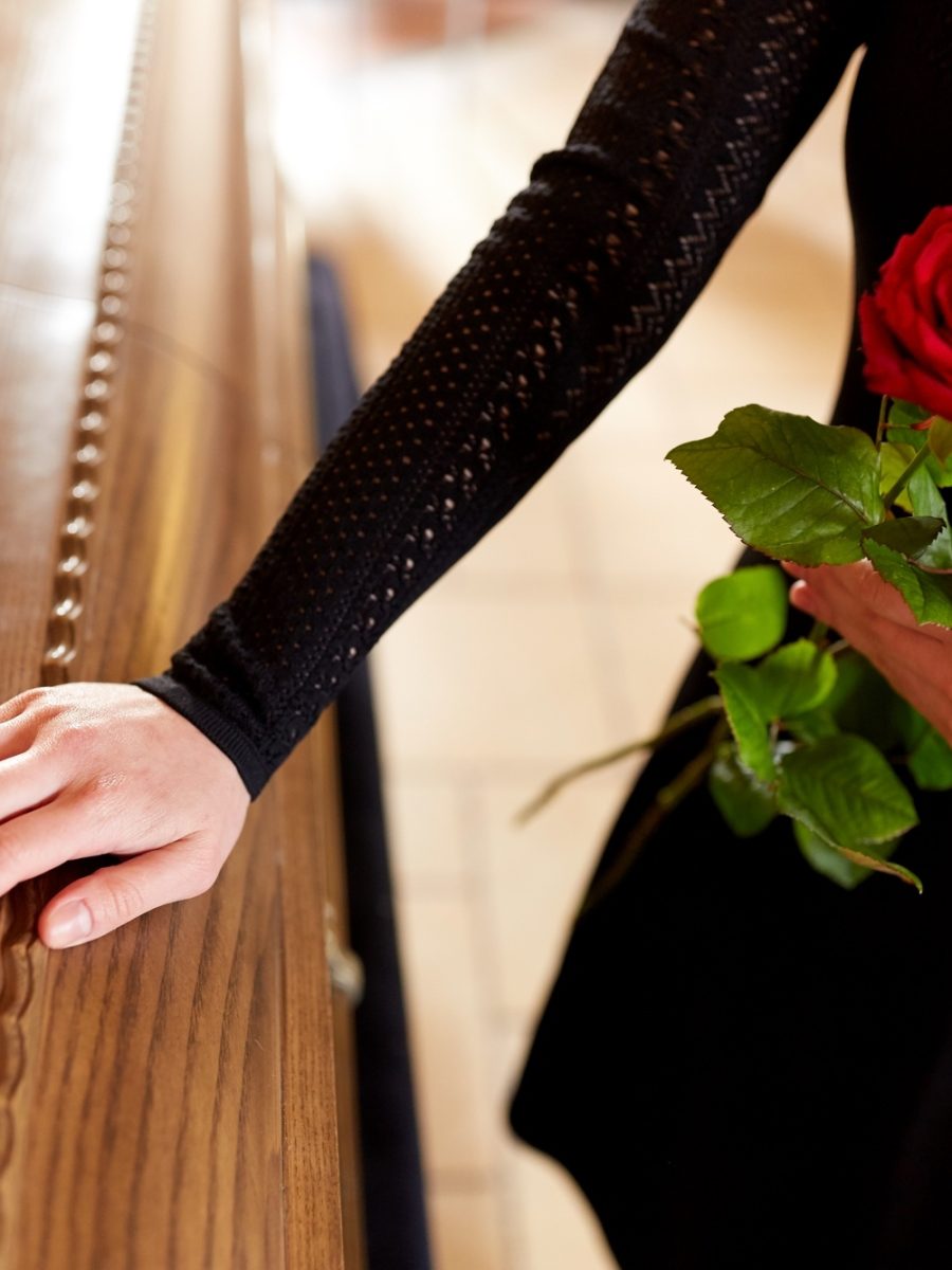 woman with red roses and coffin at funeral
